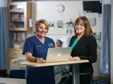 A nurse and nurse leader smile and stand together.